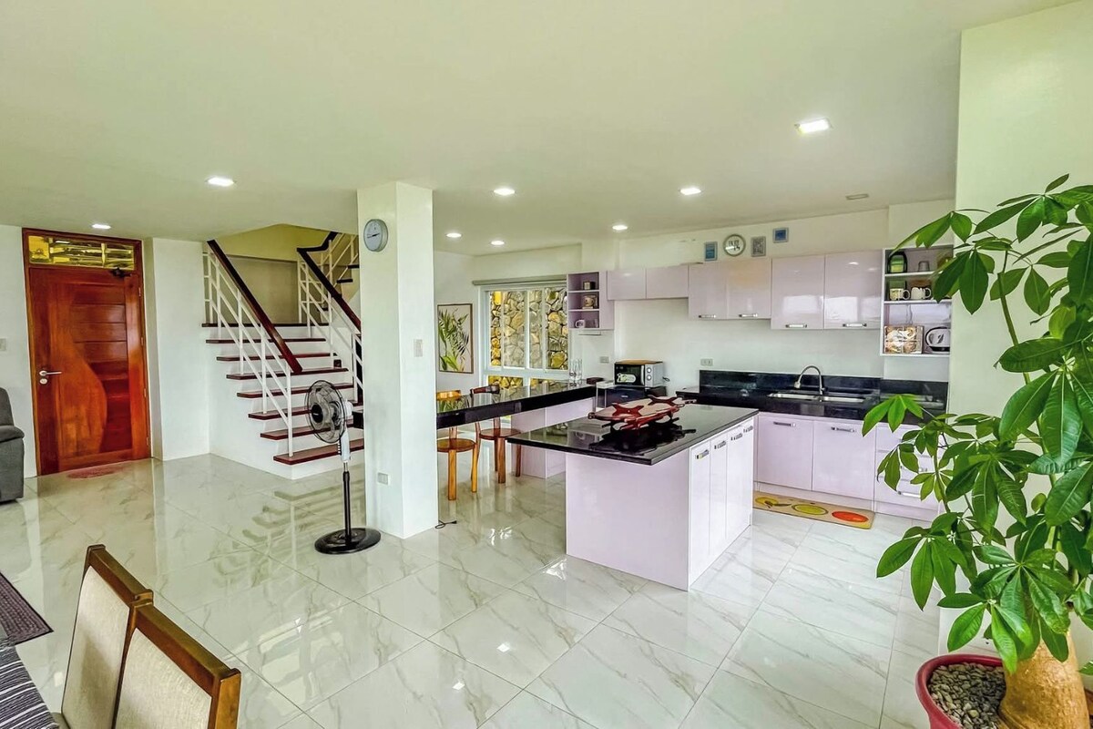A modern kitchen with white cabinets, a central island, and a dining area with a sofa and chairs.