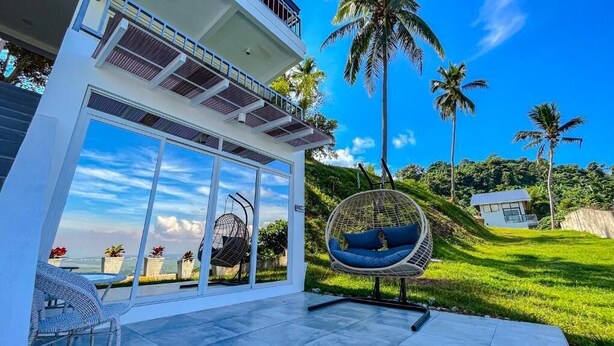 Ein modernes Haus mit großen Glasüren, einem Hängestuhl und Blick auf den Ozean.