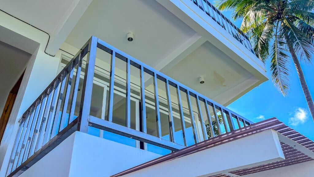 Un bâtiment moderne doté d’un balcon, de caméras de surveillance et, en arrière-plan, d’un palmier.