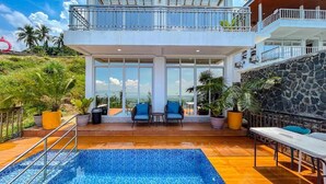 Ein moderner Poolbereich im Freien mit Blick aufs Meer, zwei Liegestühle und Kübelpflanzen.