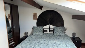 Ein Schlafzimmer mit einem Bett, zwei Nachttischen, einem großen Spiegel und einem Deckenventilator.