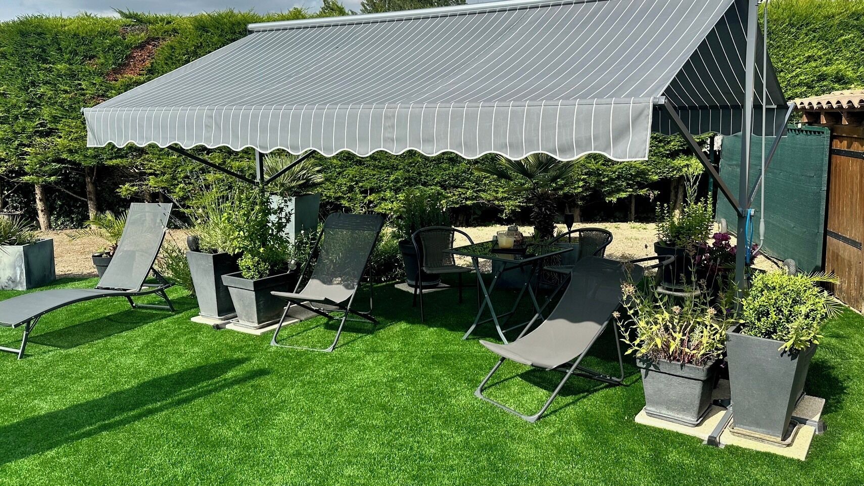 Un espace patio doté d’un coin salon abrité, de mobilier d’extérieur et de plantes en pot.