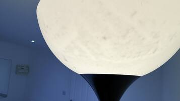 A room with a bed, a nightstand, and a lamp with a large, round, white shade.