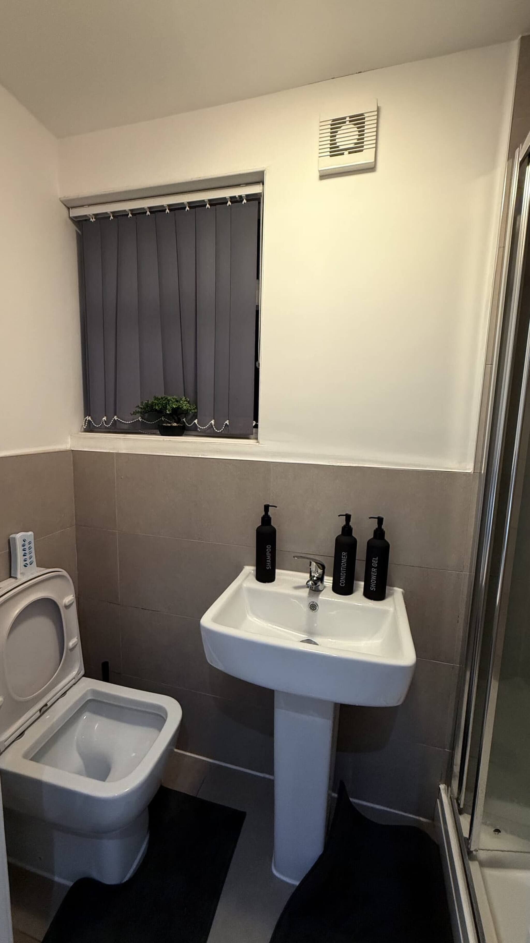 Une salle de bain équipée de toilettes, d’un lavabo et d’une fenêtre avec des rideaux.