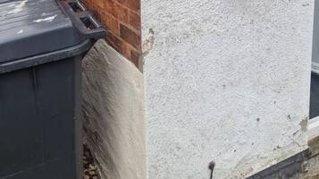 A mailbox attached to a brick wall and a black trash bin next to it.