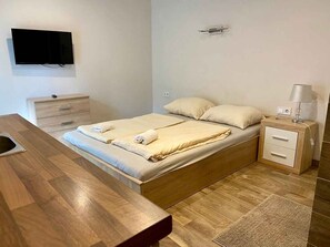 A bedroom with a bed, bedside table, lamp, and a TV mounted on the wall. - Studio with pool, hot tub and sauna near the free beach (Siófok)