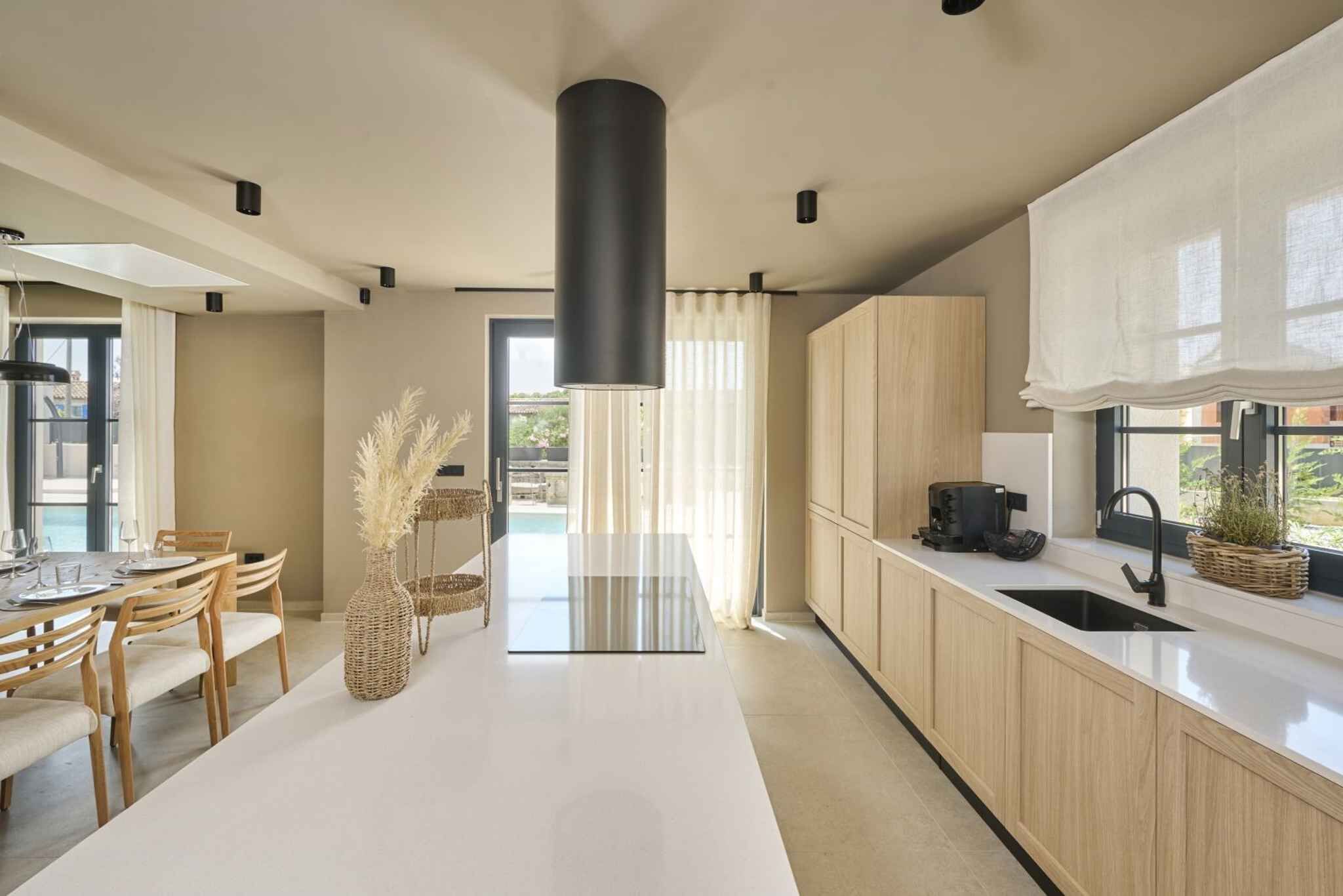 A modern kitchen with a central island, wooden cabinets, and a large window.