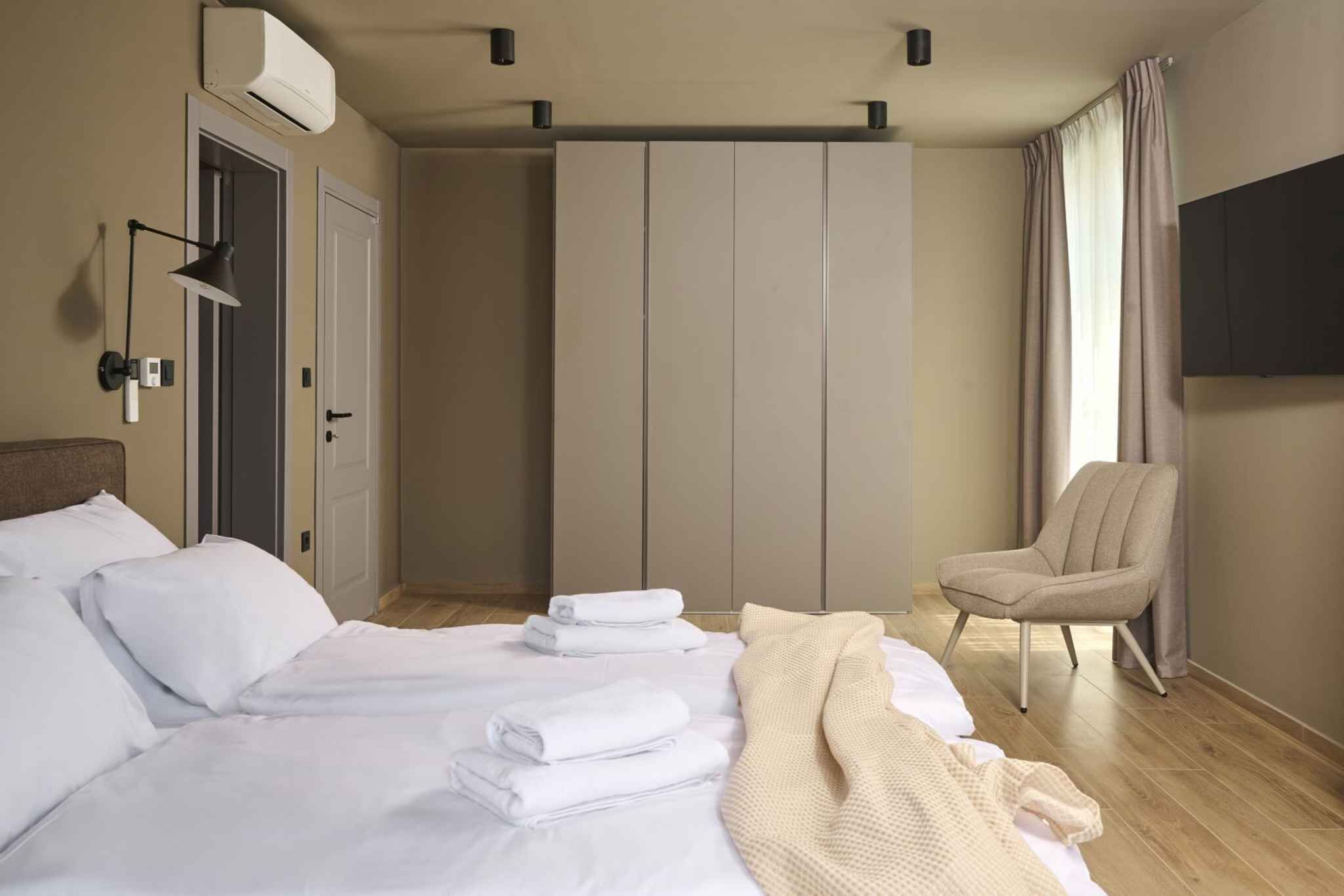 A hotel room with a bed, a chair, a wardrobe, and a TV.