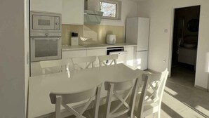 Una cocina moderna con armarios blancos, una mesa de comedor con sillas y un ventanal que proporciona luz natural.