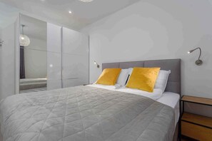 Une chambre à coucher moderne avec un grand lit, deux oreillers jaunes, une tête de lit grise et une table de chevet avec une lampe.