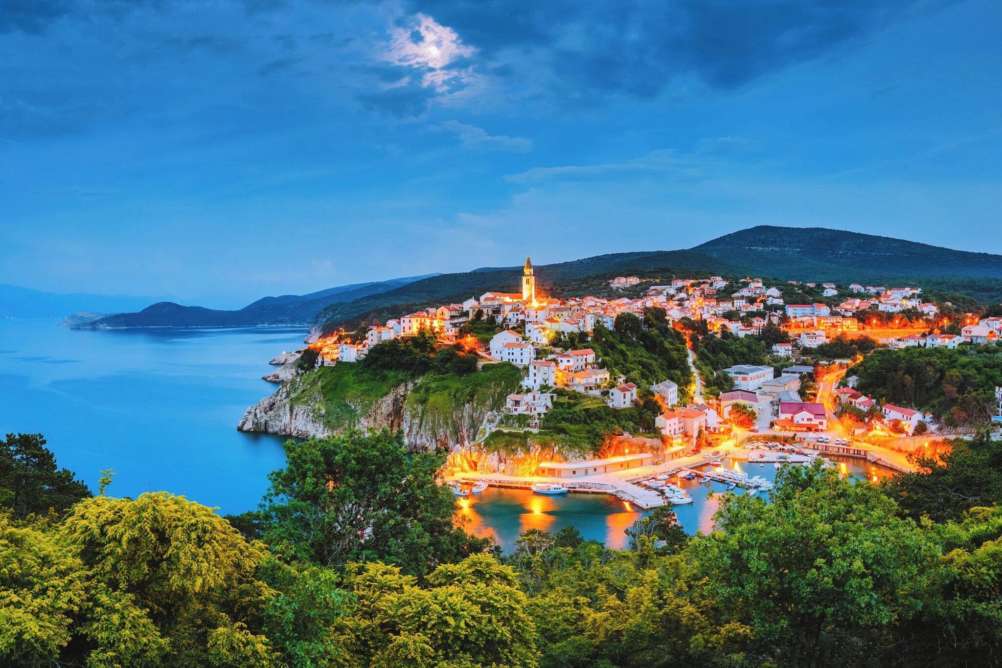 A coastal town with a prominent tower, a marina, and buildings on a hillside.