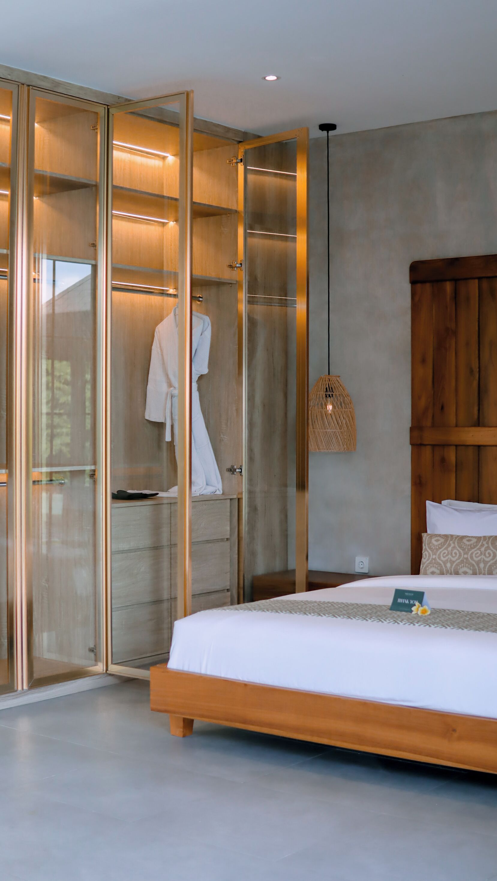 A bedroom with a wooden bed, a glass-enclosed walk-in closet, and a hanging light fixture.