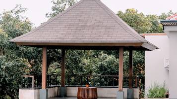 A covered pool area with a gazebo, surrounded by a tiled deck and lush greenery.