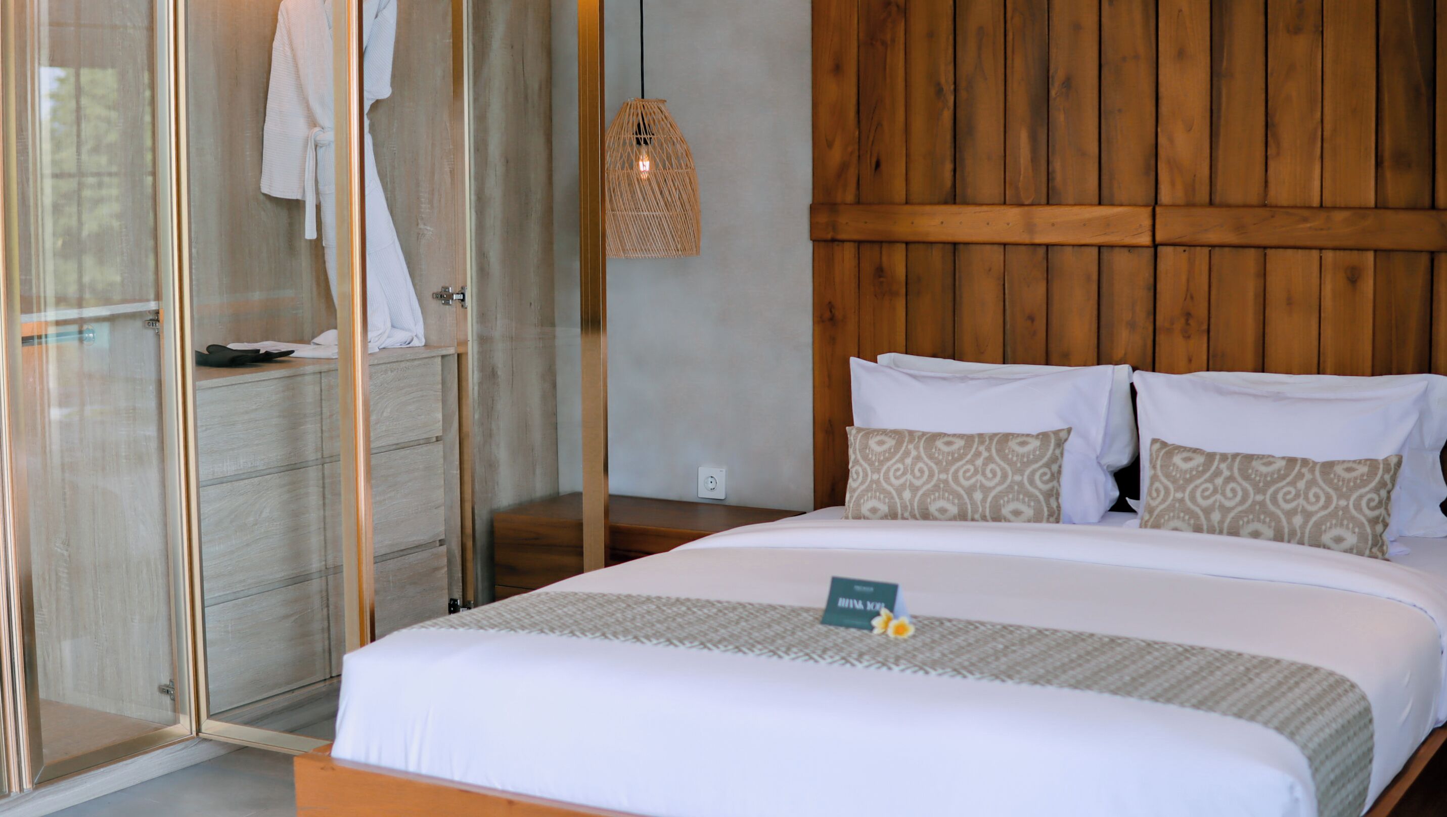 A hotel room with a bed, a wooden headboard, a glass shower enclosure, and a hanging light fixture.