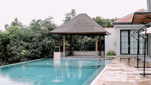 A swimming pool with a gazebo, surrounded by lush greenery.