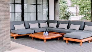 Ein Ecksofa mit vielen Kissen und einem Holztisch auf einer Terrassenfläche.