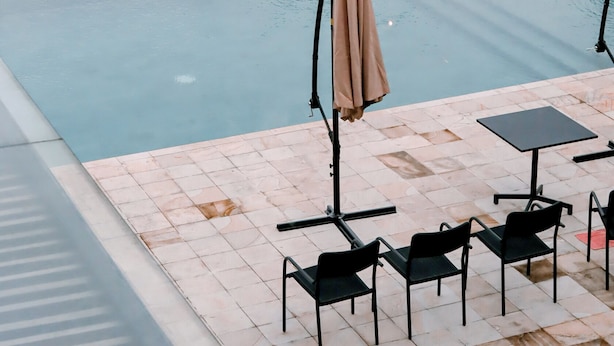 An outdoor swimming pool with a lounge area, including chairs and a table, surrounded by lush greenery.