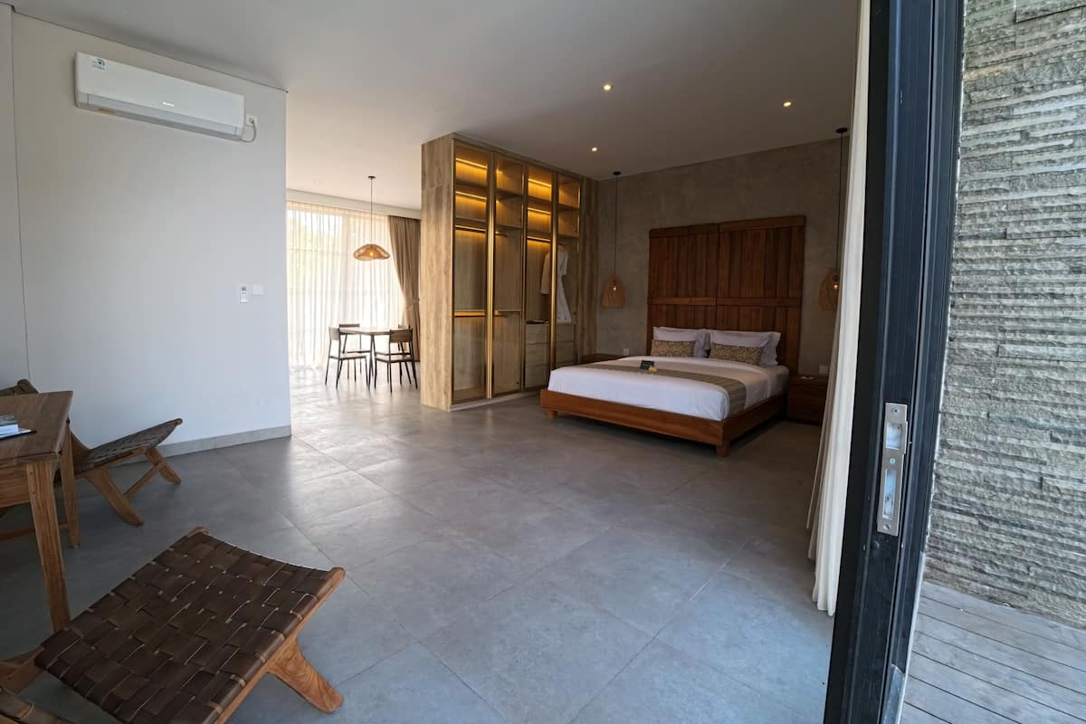 Une chambre moderne dotée d’un grand lit, d’une armoire en bois, d’un coin repas avec une table et des chaises, et d’un système de climatisation intégré.