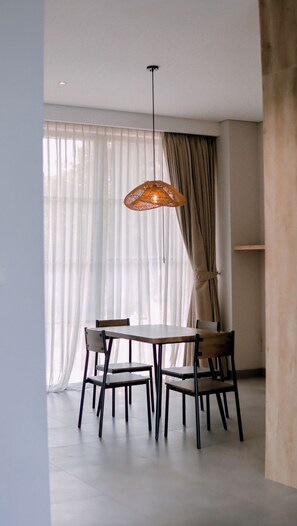 Een eethoek met een tafel, stoelen, een hanglamp en dunne gordijnen.