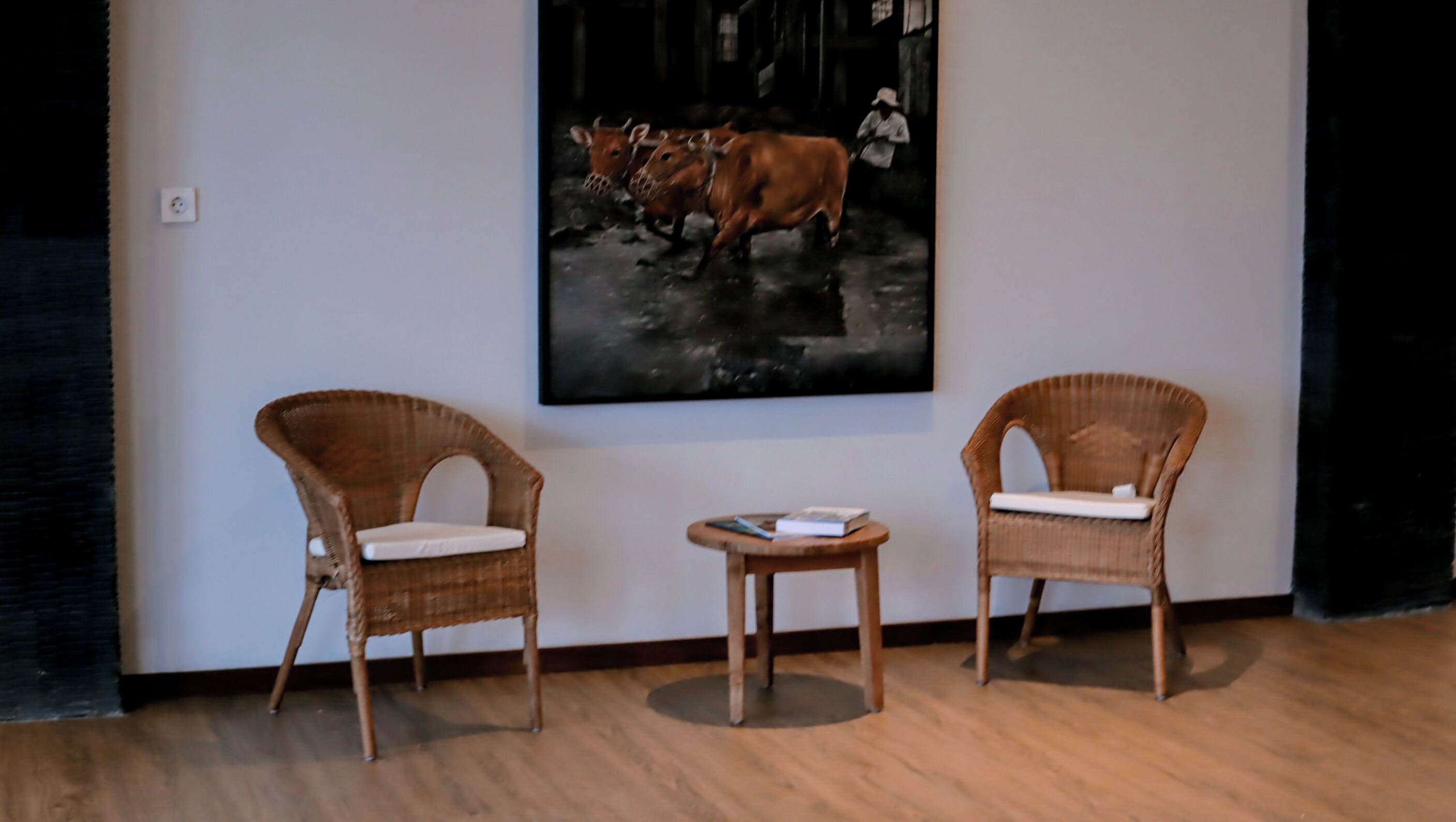 Two wicker chairs with cushions, a small round table, and a framed artwork on the wall.