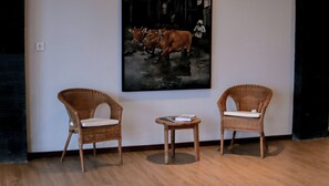 Zwei Korbstühle mit Kissen, ein kleiner runder Tisch und ein gerahmtes Kunstwerk an der Wand.
