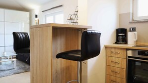 Una cocina moderna con una isla de madera, dos taburetes negros, una cafetera y un lavavajillas.