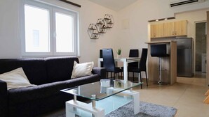 Una sala de estar moderna con una mesa de centro de vidrio, un sofá oscuro y una zona de comedor con una mesa blanca y sillas negras.