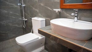 Une salle de bain avec des toilettes blanches, un lavabo blanc avec un miroir au-dessus, et un espace douche.