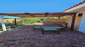 Un patio al aire libre con mesa y bancos de madera, una pérgola arriba y piso de ladrillo.
