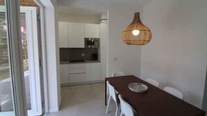 Une cuisine moderne avec des meubles blancs et un four à micro-ondes. On y trouve une table à manger avec des chaises et un luminaire suspendu.