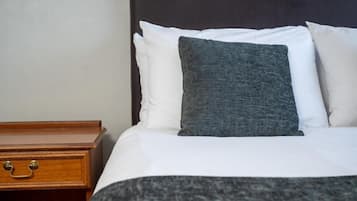 A neatly made bed with white and gray bedding, a wooden nightstand with a drawer, and a dark headboard.