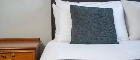 A neatly made bed with white and gray bedding, a wooden nightstand with a drawer, and a dark headboard.