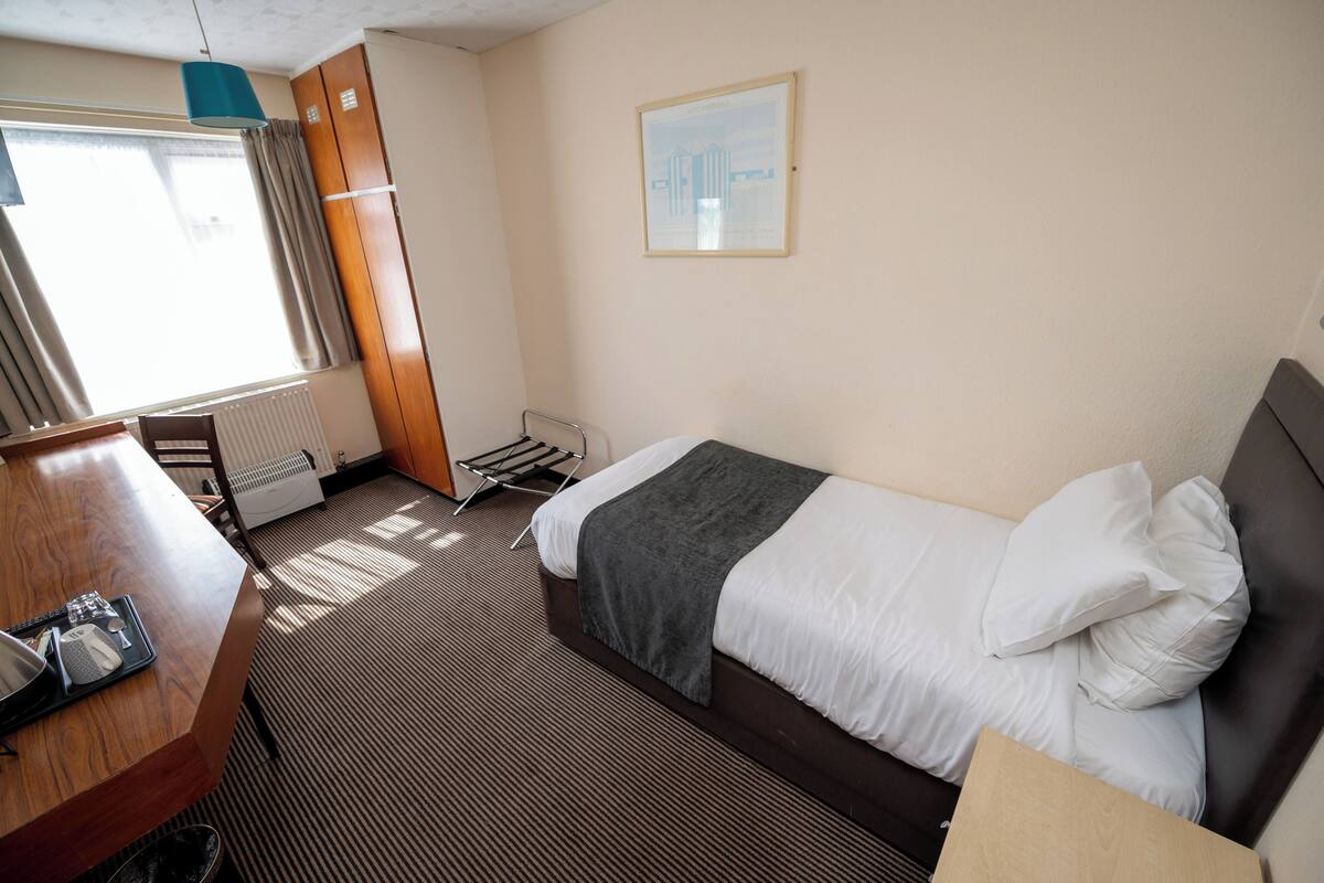 A hotel room with a bed, a desk, a radiator, and a window with curtains.