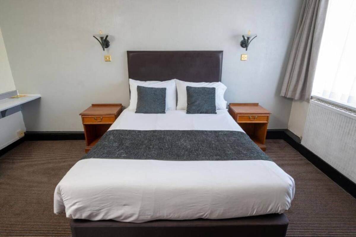 A hotel room with a large bed, two bedside tables, a nightstand, a dresser, and a window with curtains.