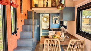 Een modern interieur met een trap, een eethoek met rieten stoelen, een welkomstbord en een uitzicht door een groot raam.