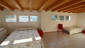Quarto com duas camas, uma escrivaninha e uma cadeira. Janelas oferecem luz natural.