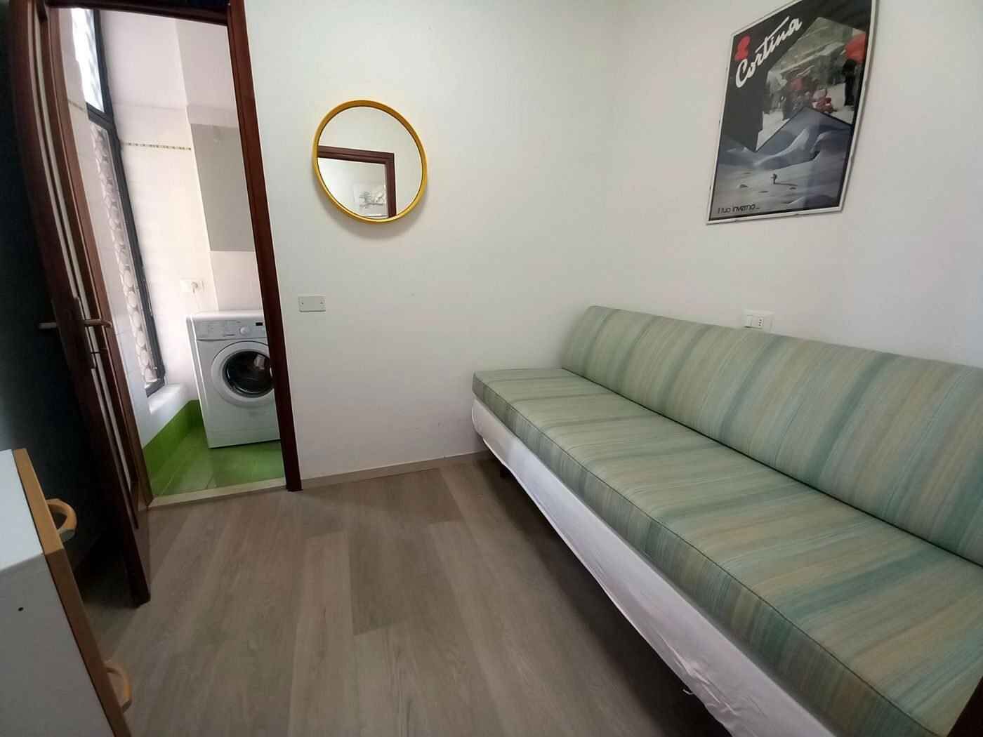 Ett litet, rent rum med en soffa, en tvättmaskin och en spegel på väggen.