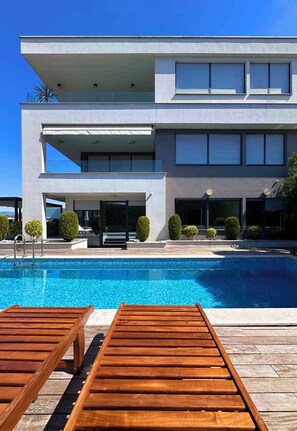 Ein modernes, zweistöckiges Gebäude mit Swimmingpool, Holzliegen und ordentlich gestutzten Büschen.