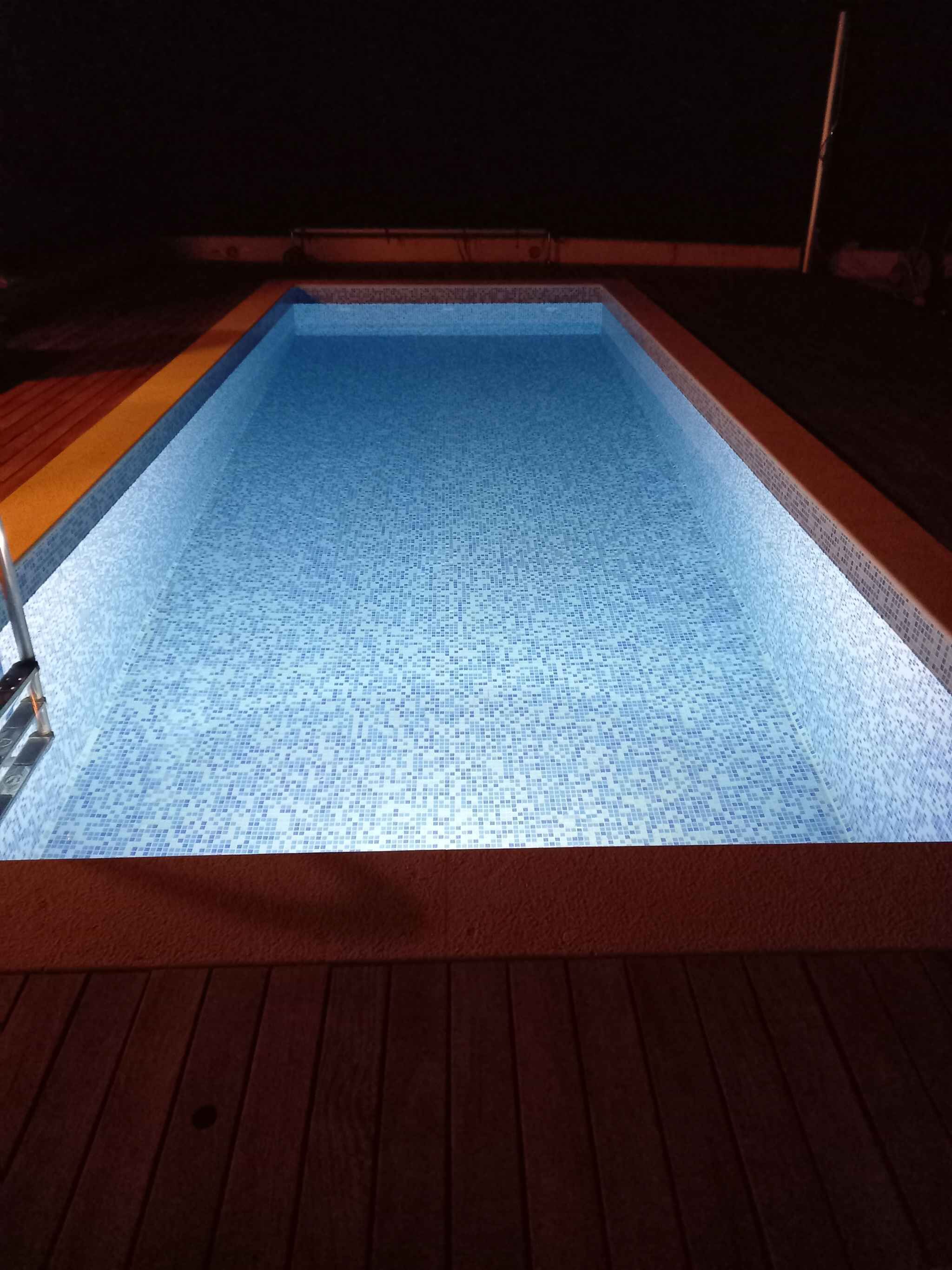 Una piscina rectangular con suelo de baldosas y un muelle de madera alrededor.
