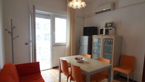 Un espacio habitable compacto con zona de comedor, un sofá, kitchenette y vistas por una puerta corredera.