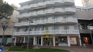 Un edificio de varios pisos con balcones, un cartel que indica una clínica privada y un letrero de taxi.