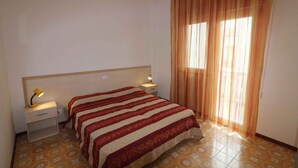 Una habitación de hotel con cama, mesitas de noche, lámpara y cortinas.