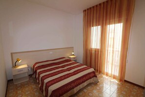 A hotel room with a bed, nightstands, a lamp, and curtains. - Holiday apartment with air conditioning and balcony (Lignano Sabbiadoro)