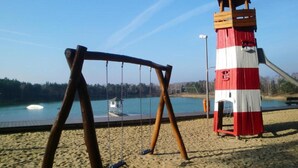 A beach with a swing set and a red and white lighthouse in the background. - Bernsteinsee Hotel and Ferien Lakeview Balcony (Sassenburg)