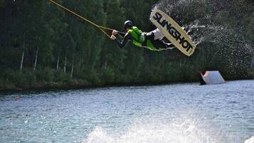 Ein Wakeboarder springt über das Wasser, sein Wakeboard trägt die Aufschrift 'SLINGSHOT'.