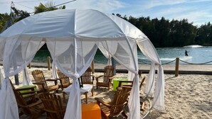 A beach cabana with a white canopy, wooden chairs, and a small orange table. - Bernsteinsee Hotel and Ferien Lakeview Balcony (Sassenburg)