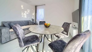 Ein modernes Wohnzimmer mit einem grauen Sofa, einem runden Esstisch mit vier Stühlen und einer Obstschale auf dem Tisch.