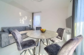 A modern living room with a grey sofa, a round dining table with four chairs, and a fruit bowl on the table. - Holiday Apartment Luxurious Relaxation – Mirna with Pool (Kornić)