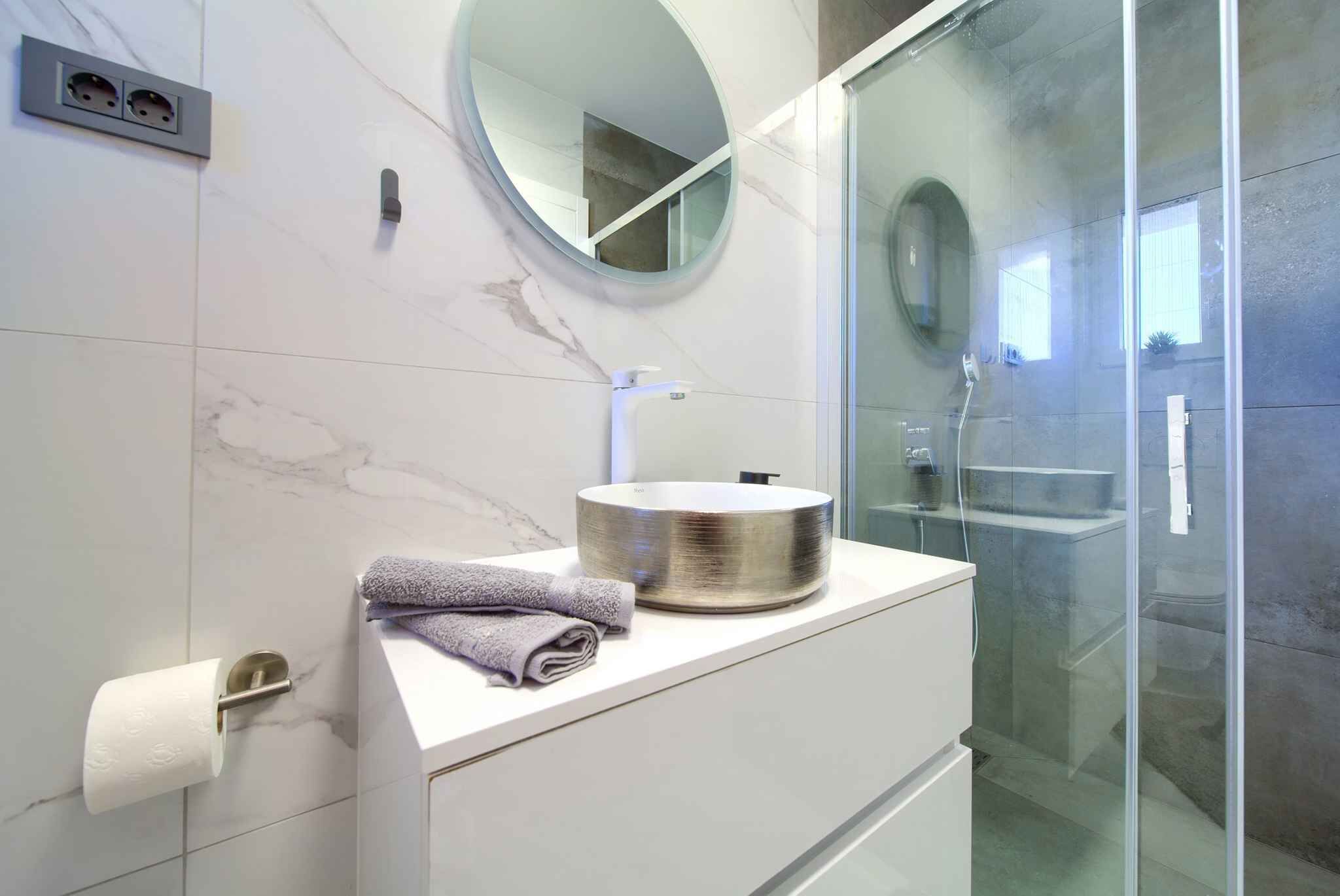 Une salle de bain moderne avec un miroir rond, un lavabo doté d’une cuve métallique et une serviette posée sur le comptoir.