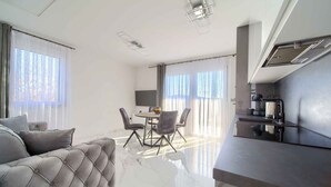 Ein modernes Wohnzimmer mit einem grauen Sofa, einem Esstisch mit Stühlen und einer Küchenzeile inklusive Kaffeemaschine.